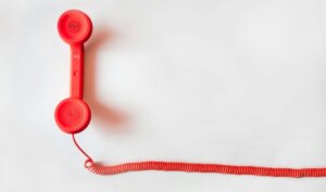 Vintage red phone handset with coiled cable on a clean white background, classic communication device.